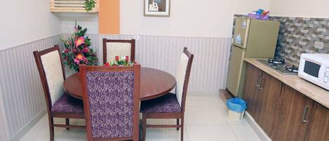 A dining area with a round table and four chairs, a refrigerator, and a microwave on the adjacent counter.