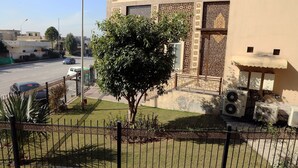 A building with a decorative facade, a tree in the front yard, and parked cars. - Hak Mall Suites (Rawalpindi)