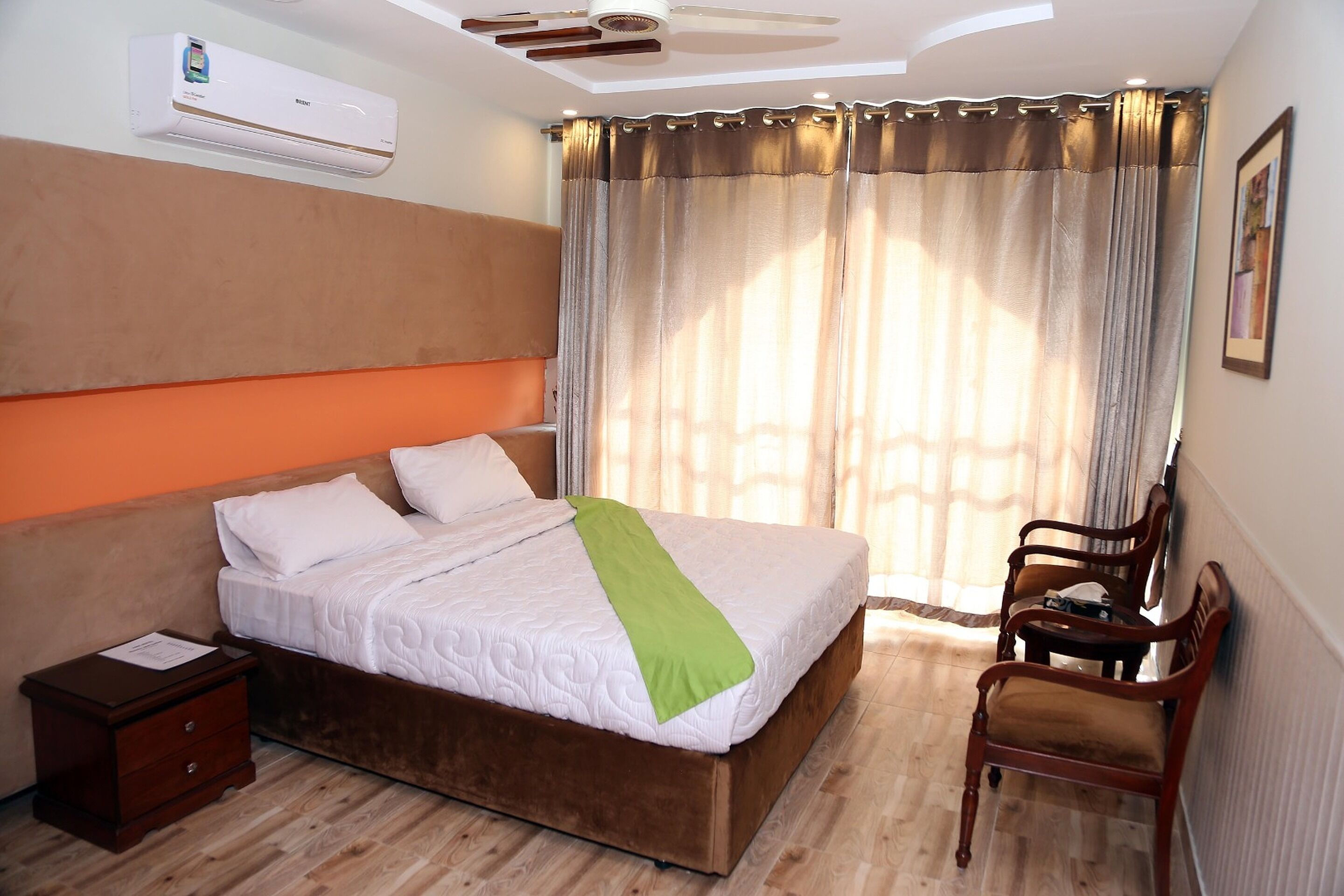 A hotel room with a bed, a nightstand, a chair, and a window with curtains.