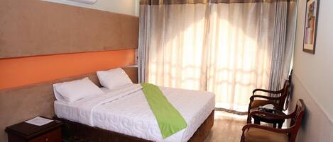 A hotel room with a bed, a nightstand, a chair, and a window with curtains.