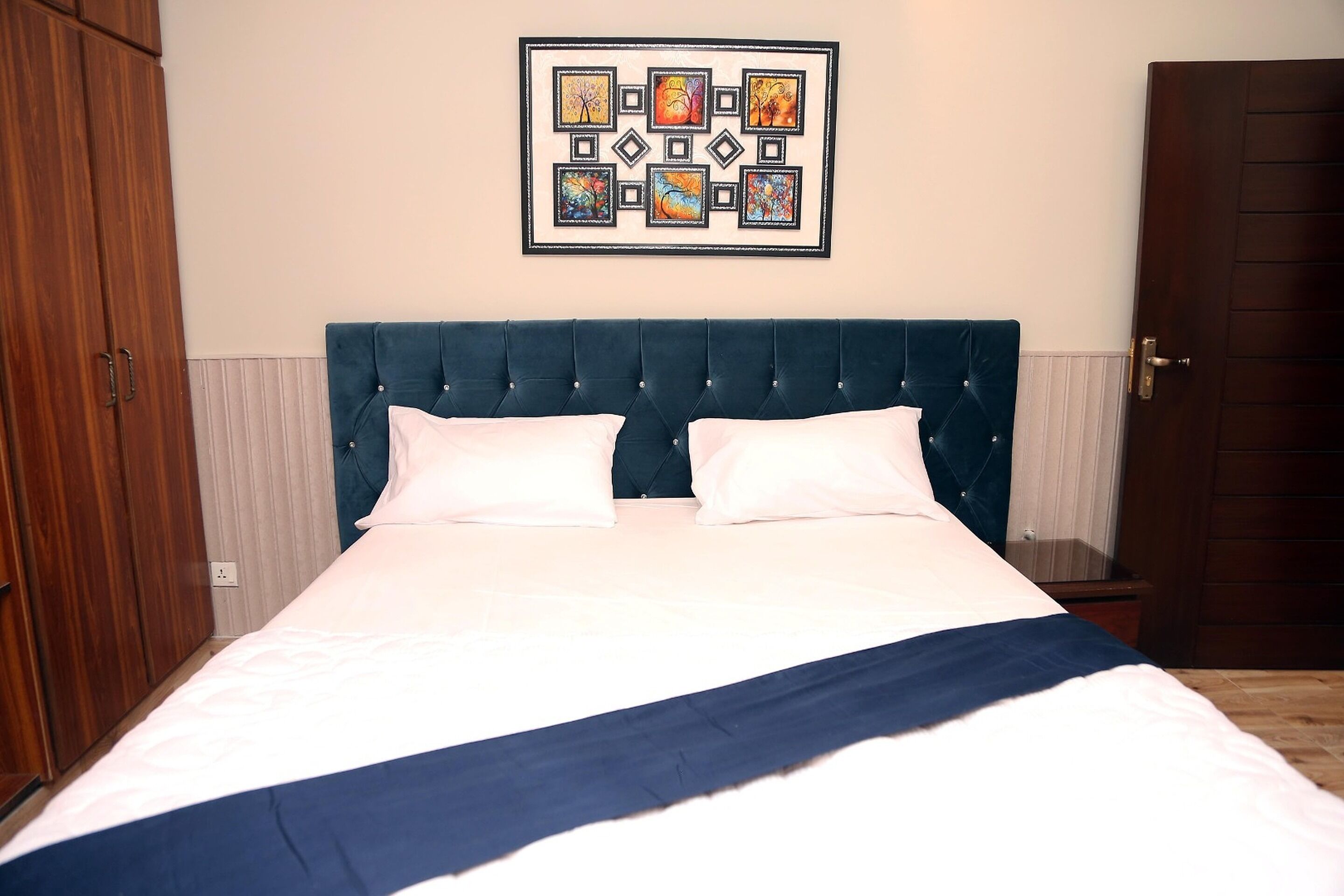 A bedroom with a large bed, a dark blue headboard, and a wall-mounted artwork.