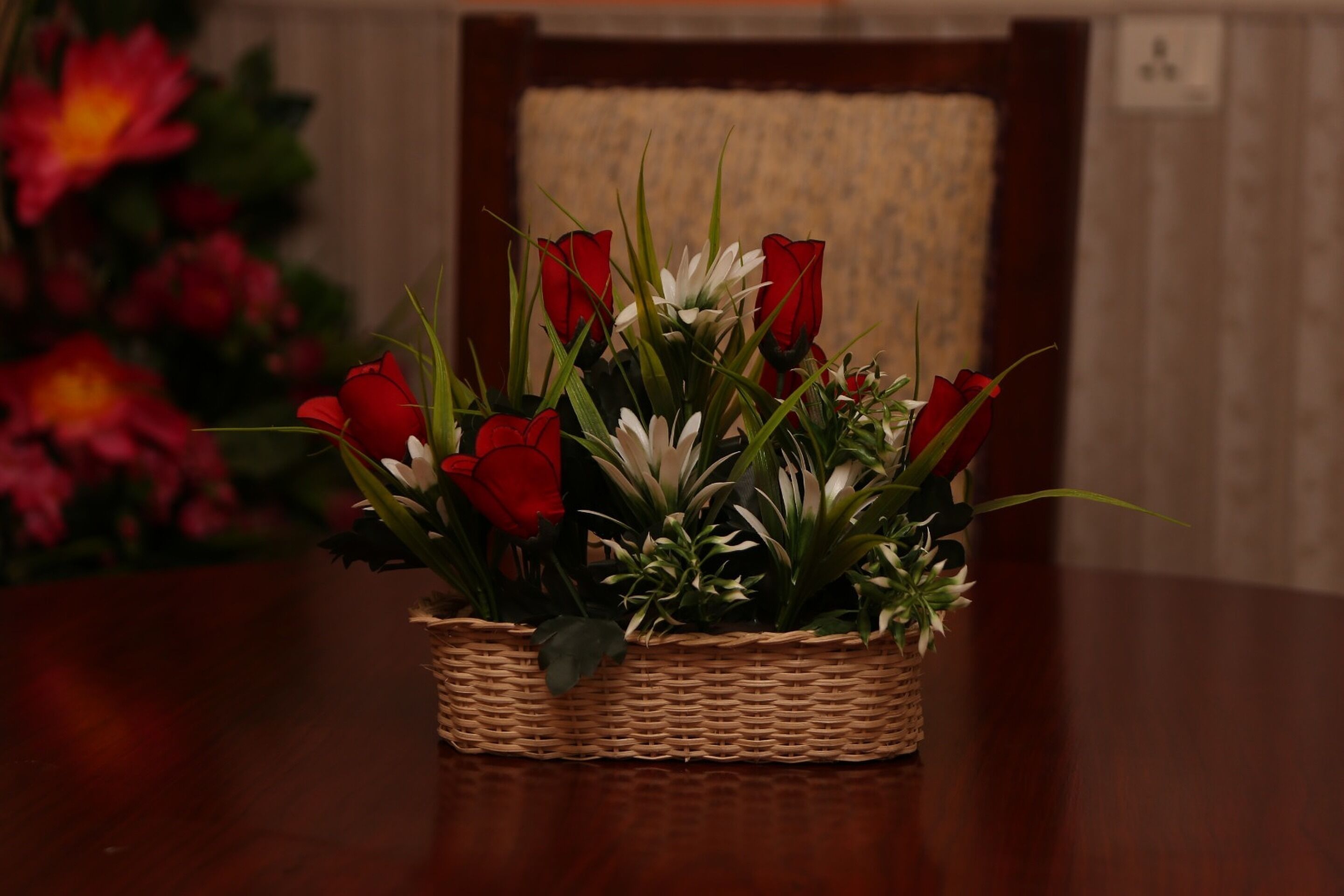 A wicker basket with red and white flowers on a wooden table.