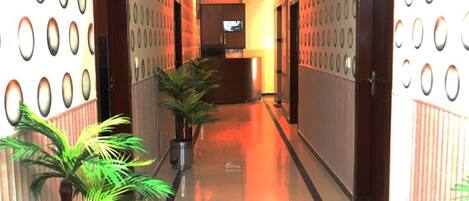 A hotel corridor with a polished floor, potted plants, a reception desk, and patterned walls.