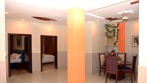 A hotel room with a bed, a desk, and a chair. There is a window with curtains, a ceiling fan, and a light fixture. - Hak Mall Suites (Rawalpindi)