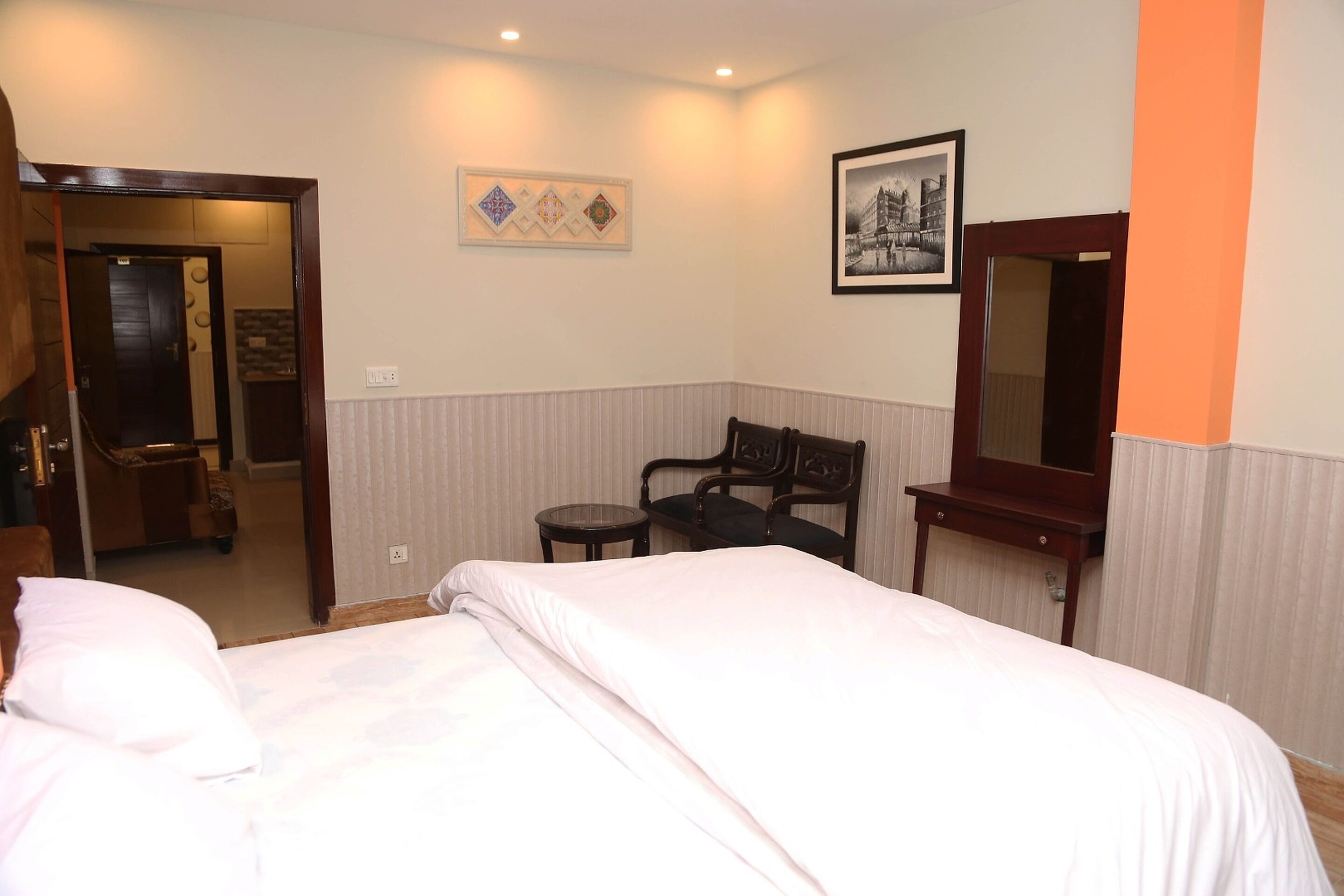 A hotel room with a bed, a chair, a small table, a mirror, and artwork on the walls.