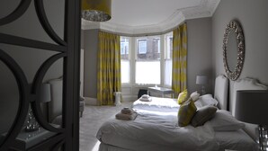 Ein Hotelzimmer mit zwei Betten, einem großen Fenster mit gelben Vorhängen, einer Kristallleuchtre und einem dekorativen Spiegel an der Wand.