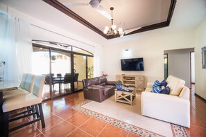 A living room with a sofa, a coffee table, a TV, and a dining area with a table and chairs.