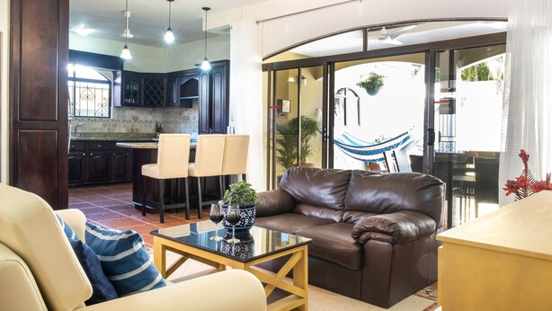 Een woonkamer met een leren bank, een glazen salontafel, en een eethoek met stoelen, met een keuken op de achtergrond.