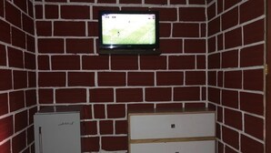 Una habitación con pared de ladrillo, televisor montado, un refrigerador pequeño y un armario de madera.
