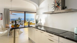 Een moderne keuken met witte kasten, een zwart aanrecht en uitzicht op de oceaan.