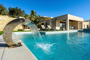 A swimming pool with a modern water feature, lounge chairs, and a stone wall.
