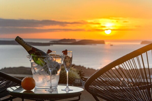 A sunset view with a bottle of champagne, glasses, and an orange on a table.
