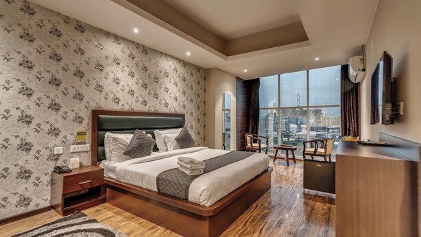 A modern hotel room with a large bed, a desk, and a view of the cityscape. - Hotel Golden Leaf Kashmir (Srinagar)