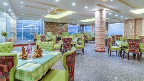 A spacious restaurant with green upholstered chairs and tables, brick walls, and large windows. - Hotel Golden Leaf Kashmir (Srinagar)