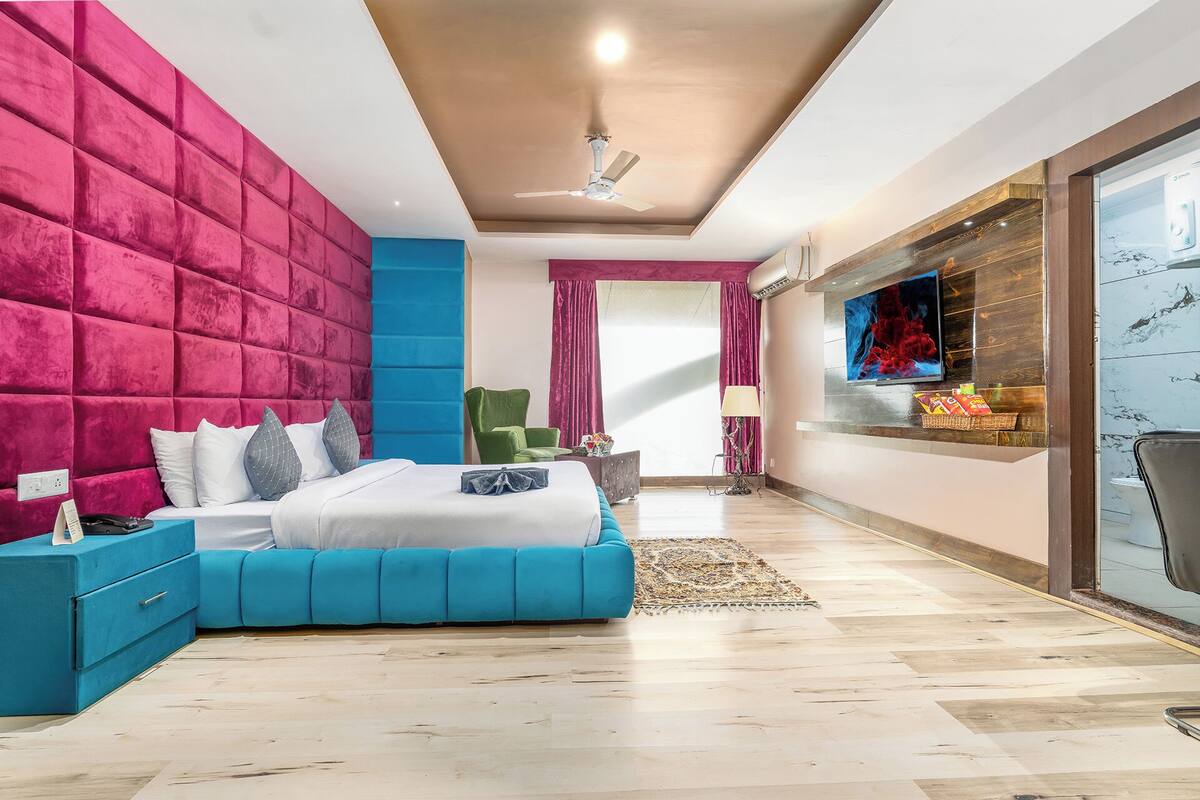 Un dormitorio moderno con una cama grande, ventilador de techo, televisión y puerta corrediza de cristal.