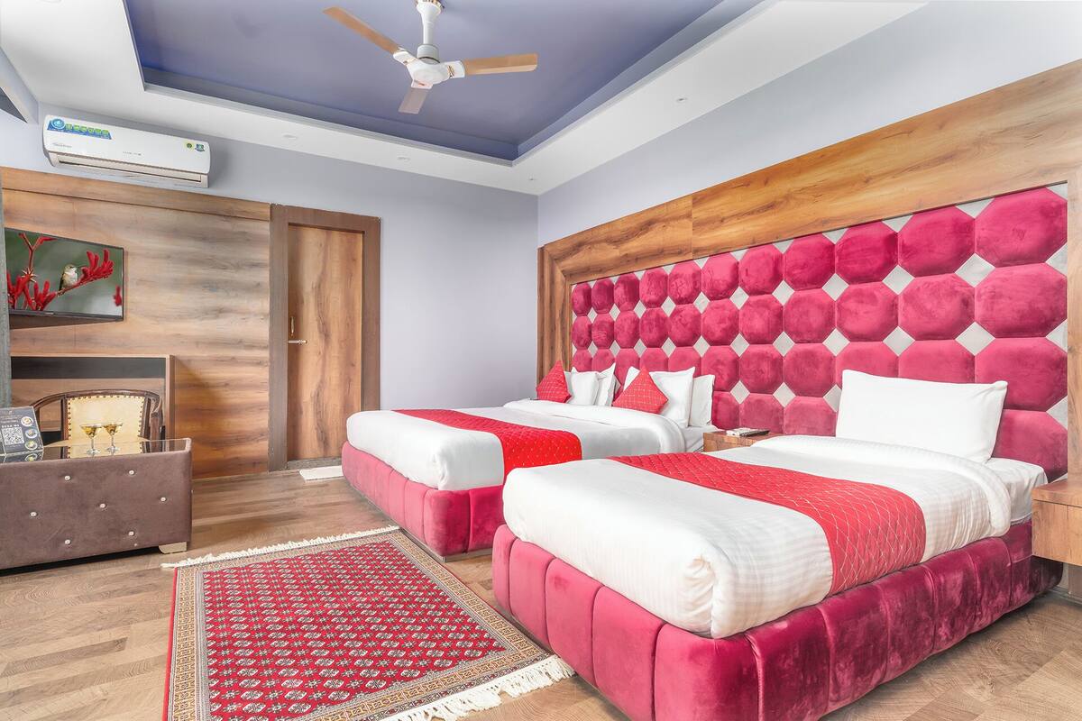 Un dormitorio moderno con dos camas, cabecero de madera, ventilador de techo y una alfombra roja estampada.