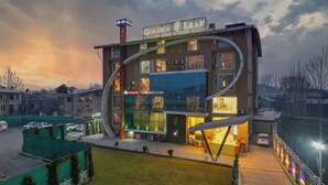 A modern hotel with a unique curved architecture, a visible restaurant, and a parking area. - Hotel Golden Leaf Kashmir (Srinagar)