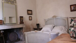 Een slaapkamer met een bed van wit wilgentenen, een grote spiegel, een klein tafeltje met een lamp en een decoratieve vaas.