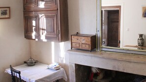 Een kamer met een houten kast, een tafel met een kantkleed, een stoel, een spiegel met een decoratieve lijst, en een klein krukje.