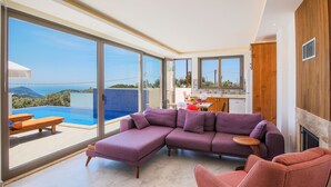 A modern living room with a purple sofa, a red chair, and a view of a swimming pool and mountains.