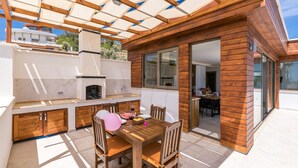 An outdoor kitchen area with a wooden table and chairs, a pizza oven, and a dining table set for two.