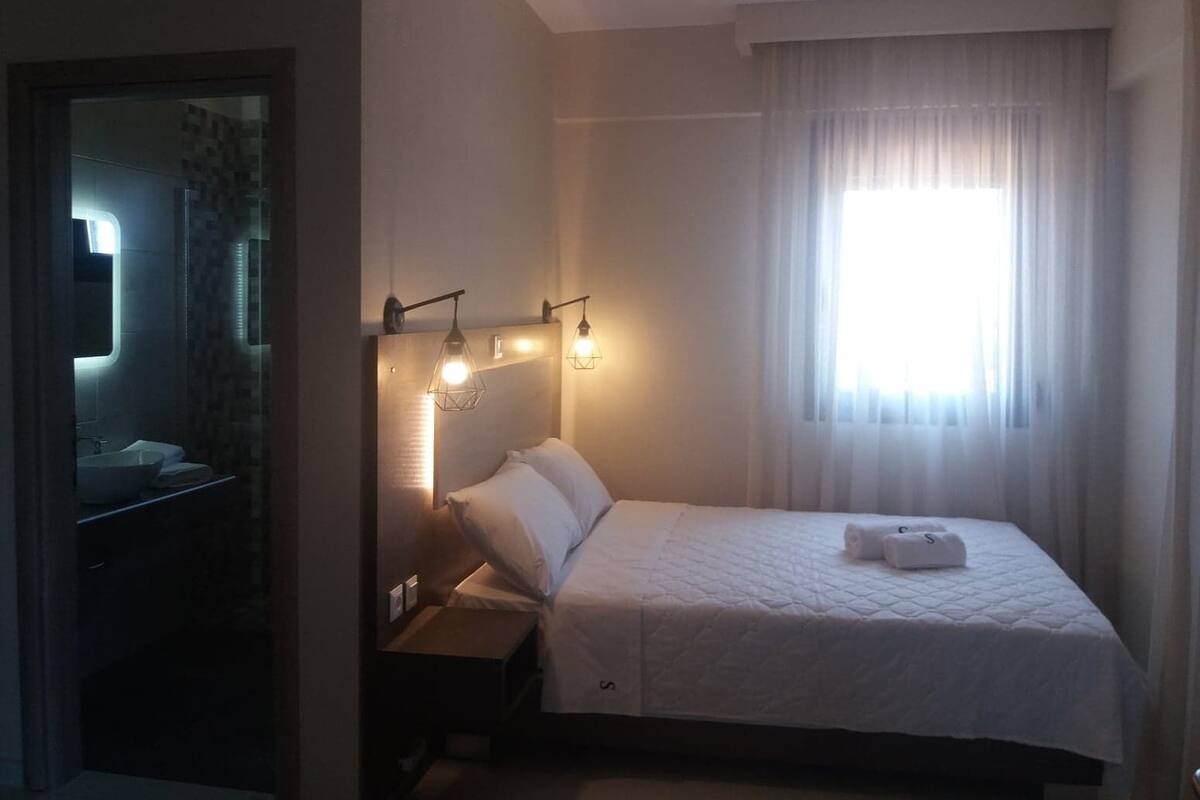 Ein Hotelzimmer mit Bett, Nachttisch, Spiegel und einem Fenster mit Vorhängen.