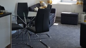 Uma sala de estar moderna com uma mesa de jantar de vidro, cadeiras pretas, um sofá e uma janela com cortinas.