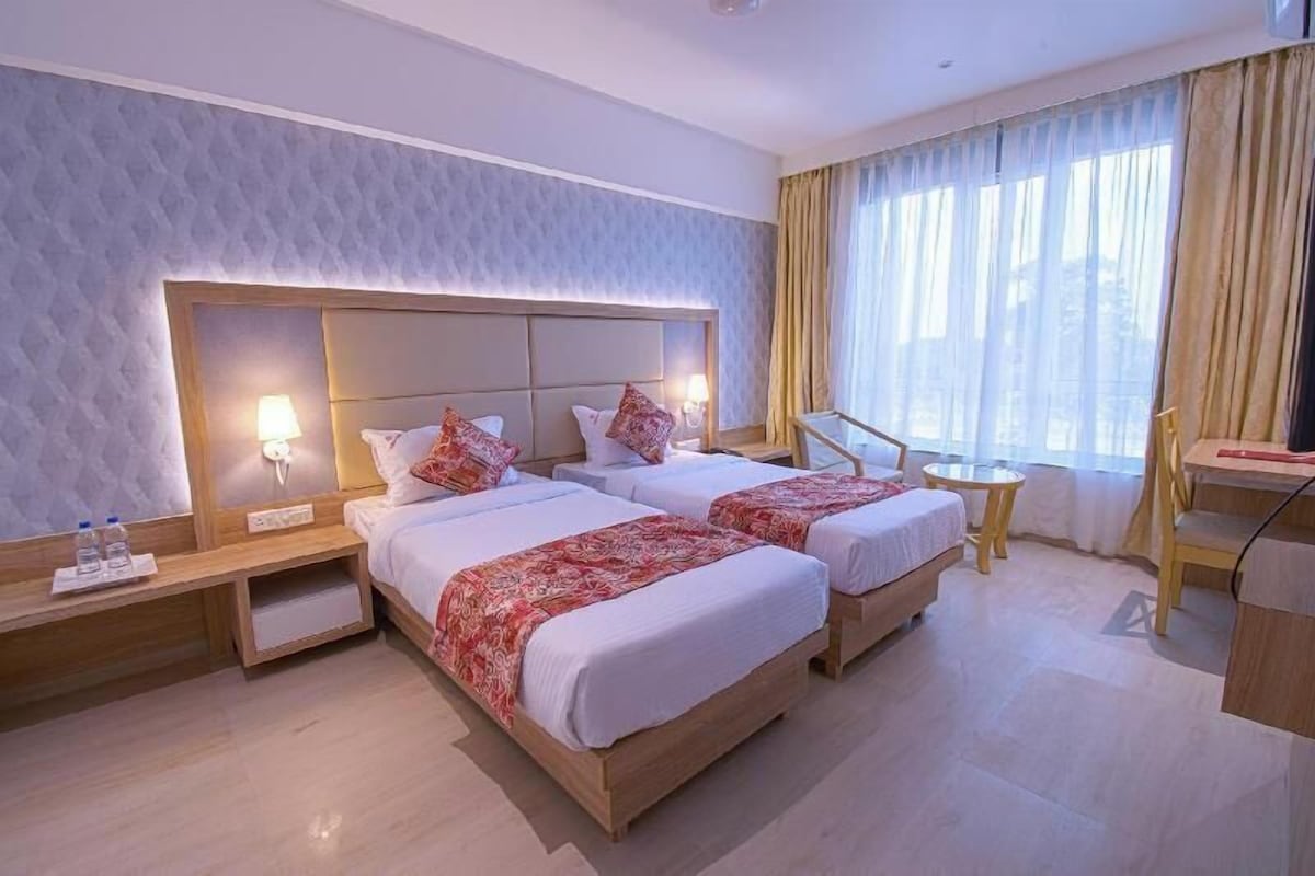 A hotel room with two beds, a desk, a chair, a small table, and a window with curtains.