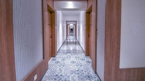 A long, narrow hallway with wooden doors on both sides and a patterned tile floor. - Hotel Park Tree (Kolhapur)