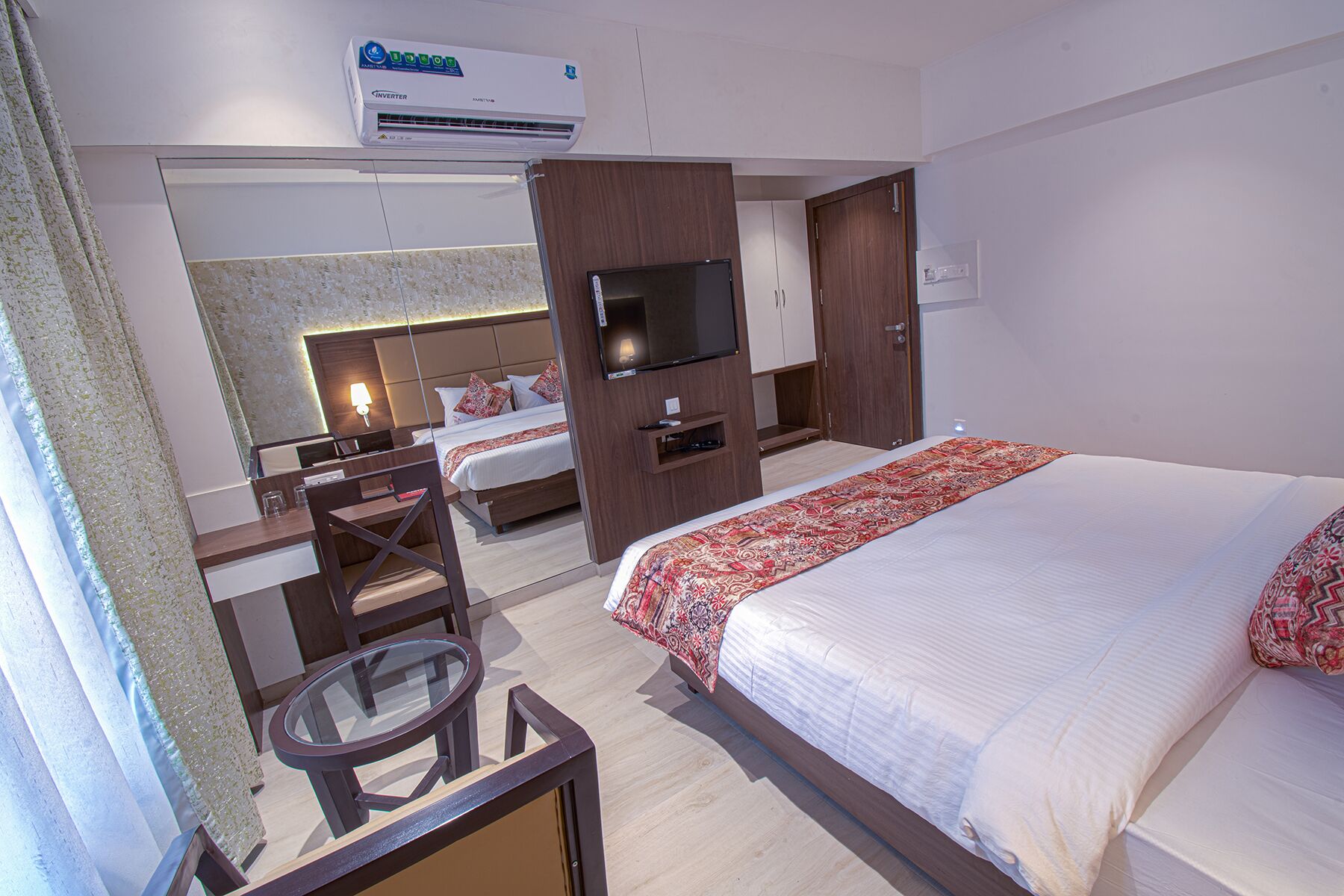 A hotel room with a bed, a desk with a chair, a TV, and an air conditioner.