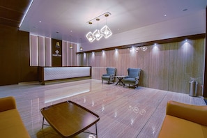 A modern hotel lobby with a reception desk, seating area, and decorative lighting.