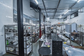 A commercial kitchen with stainless steel appliances, shelves with dishes, and a black countertop.