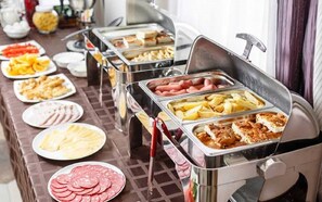 A buffet with various food options including sliced meats, fruits, and cooked items.