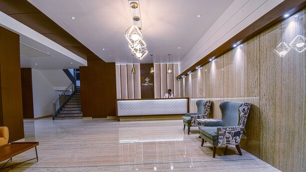 A modern hotel lobby with a marble floor, a reception desk, and two patterned armchairs. - Hotel Park Tree (Kolhapur)
