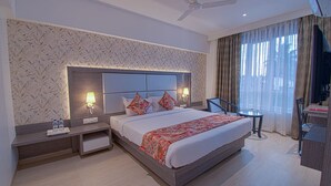 A hotel room with a large bed, two bedside tables with lamps, a ceiling fan, a TV, and a view of the outdoors through sheer curtains. - Hotel Park Tree (Kolhapur)
