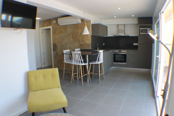 A modern kitchen with a dining area, a flat-screen TV, and a yellow chair.