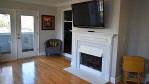 A living room with a fireplace, a television mounted above it, a chair, and a small wooden stool. - Special Pricing Uptown Condo Minutes from Bank of America Stadium (Charlotte)
