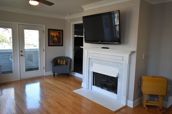 A living room with a fireplace, a television mounted above it, a chair, and a small wooden stool.