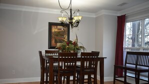A dining room with a wooden table and chairs, a chandelier, a framed picture on the wall, and a window with a view of trees. - Special Pricing Uptown Condo Minutes from Bank of America Stadium (Charlotte)