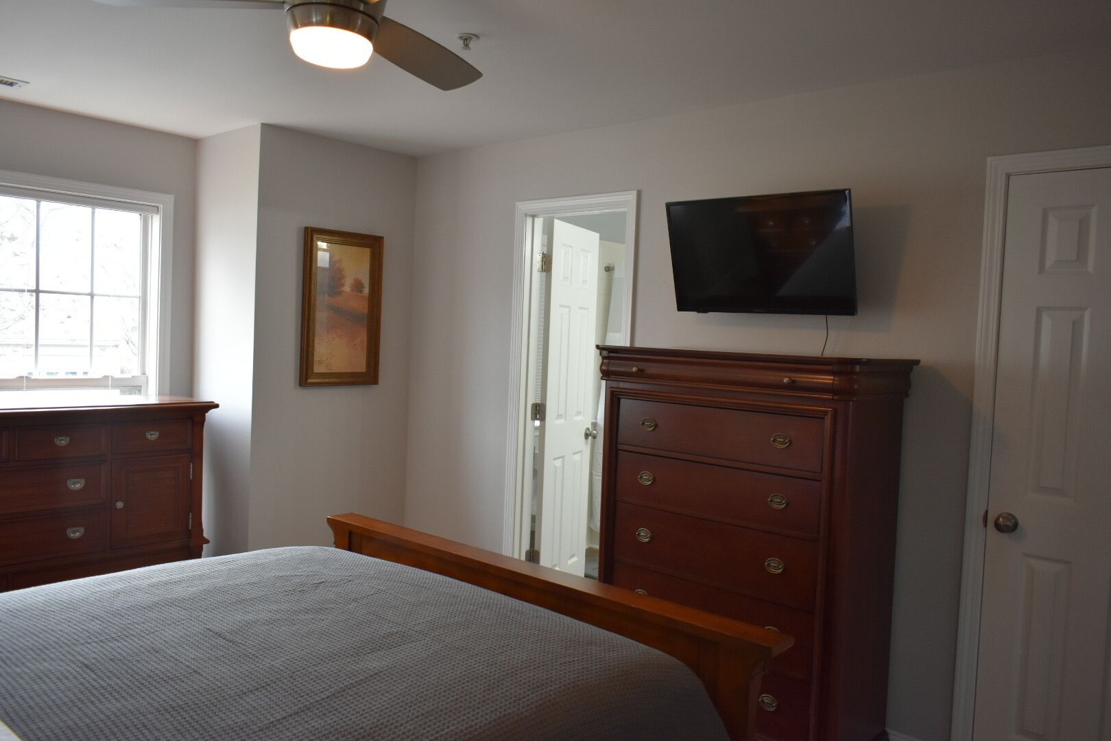 A bedroom with a bed, a dresser, a television mounted on the wall, and a window.