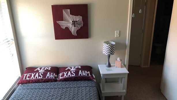Une chambre à coucher avec un lit, des oreillers, une table de chevet, une lampe et une œuvre d’art murale.