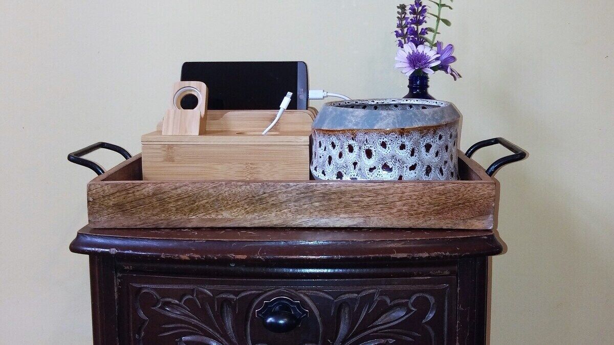 A wooden cabinet with a tray, a vase with flowers, and a black object on top.