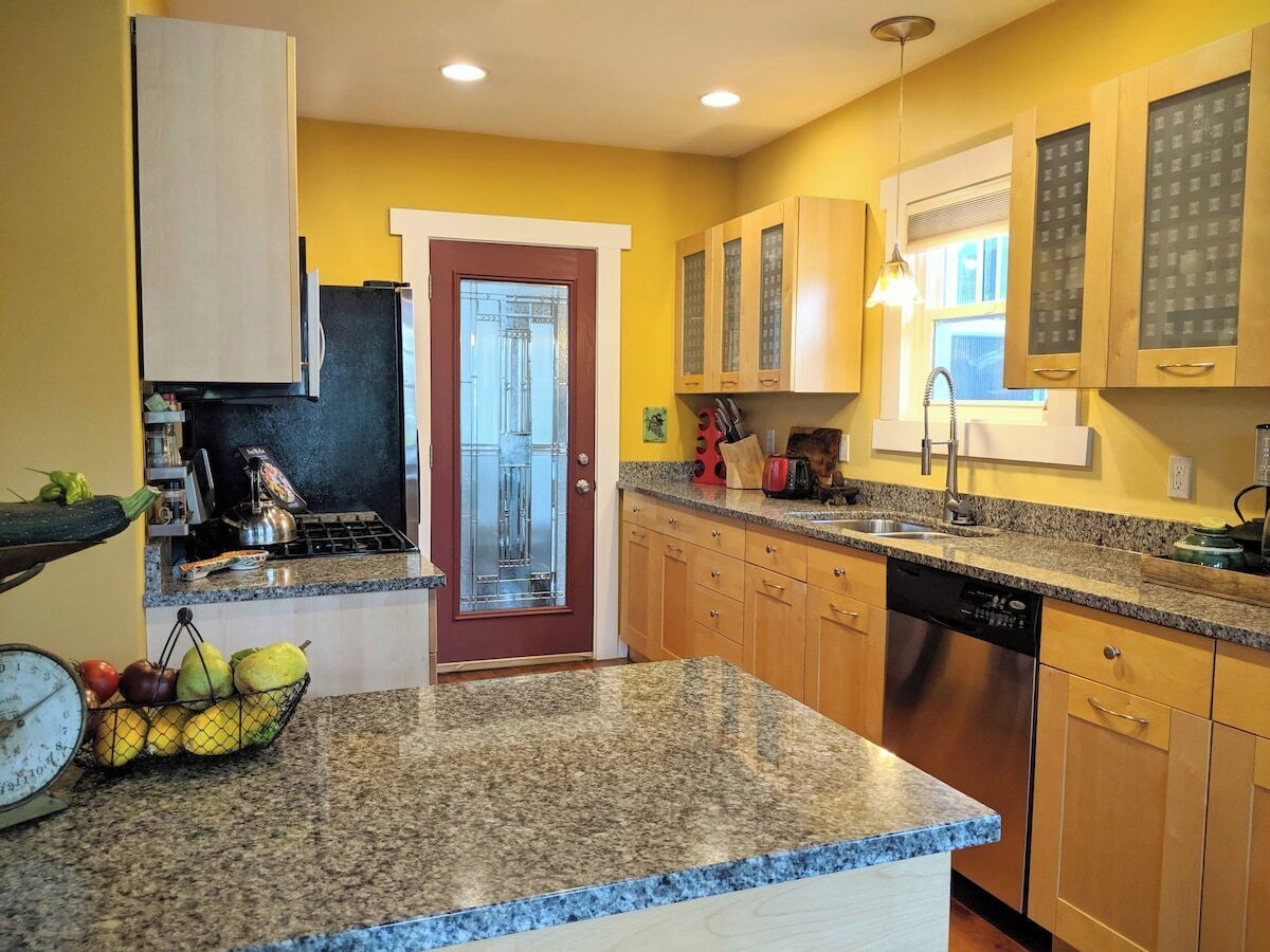 Una cocina con encimeras de granito, armarios de madera, lavavajillas y una ventana con persianas.