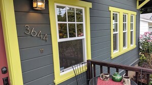 A house with a number '3644' on the side, a porch with a table and chairs, and a window with yellow trim. - Dragonfly House-One Bedroom Craftsman in Trendy Kenton (Portland)