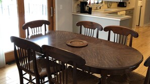 Un coin repas avec une table et des chaises en bois, un lustre et une cuisine en arrière-plan.