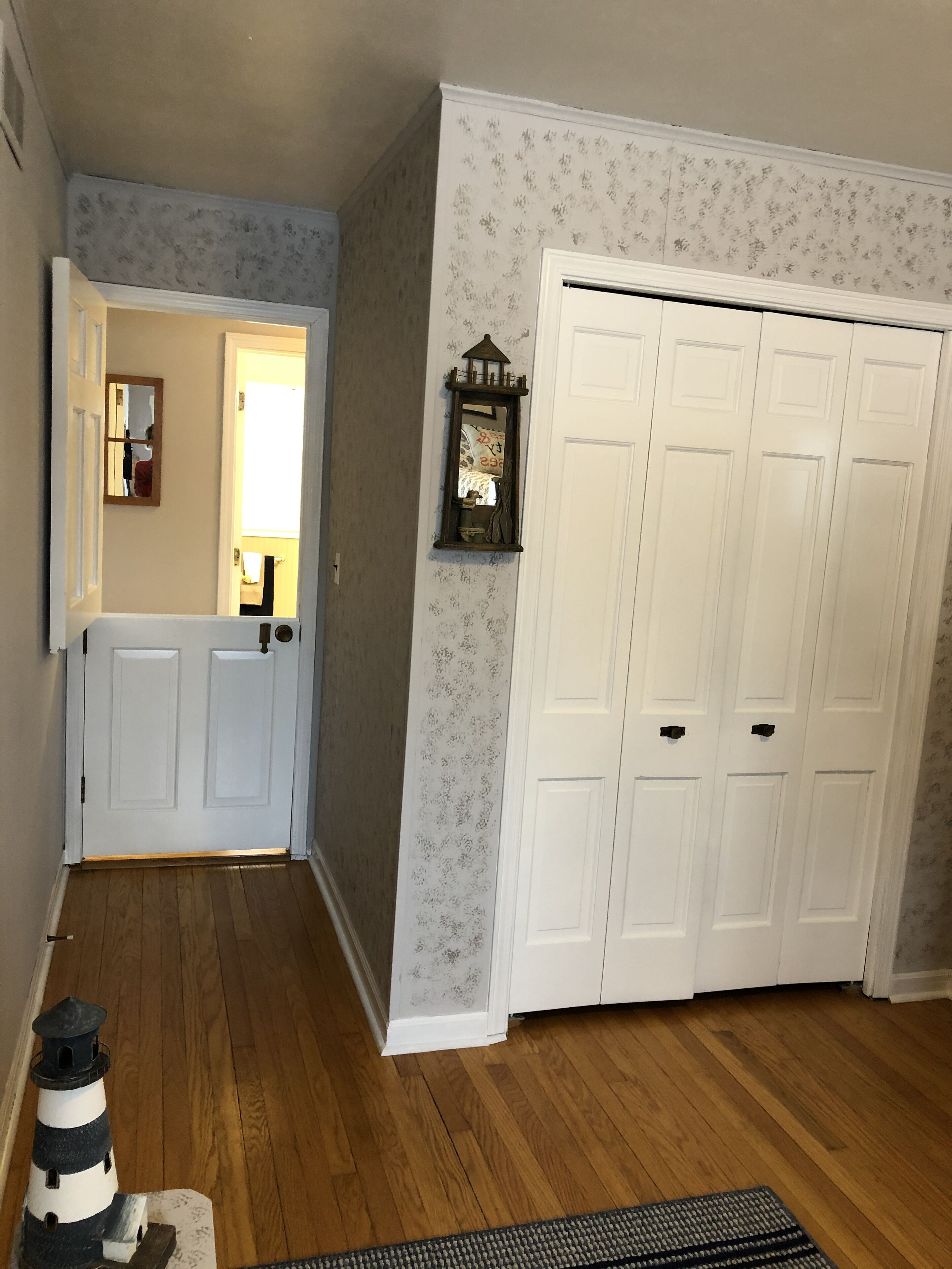 A hallway with wooden flooring, a white door, and a white closet with multiple doors.