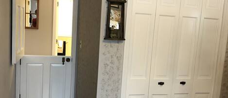 A hallway with wooden flooring, a white door, and a white closet with multiple doors.