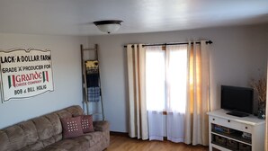 A living room with a sofa, a television on a stand, and a sign on the wall. - Country Serenity at The Resting Windmill (Mauston)