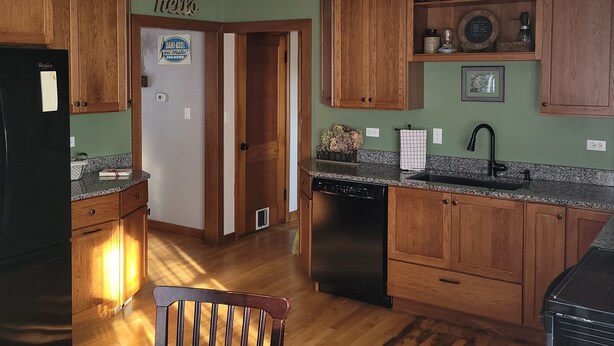 A kitchen with wooden cabinets, a refrigerator, a dishwasher, and a dining area with a table and chairs. - Country Serenity at The Resting Windmill (Mauston)