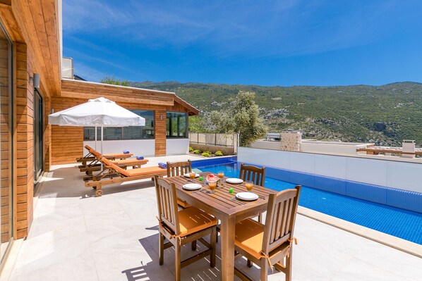 A wooden deck with a pool, lounge chairs, and a table set for dining.